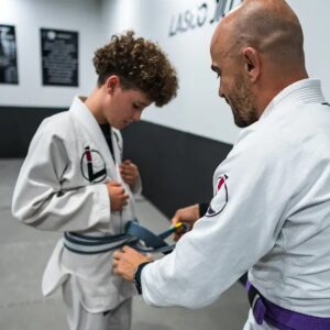 A Lasco Jiu Jitsu coach helping a young student with his BJJ belt in Varsity Lakes
